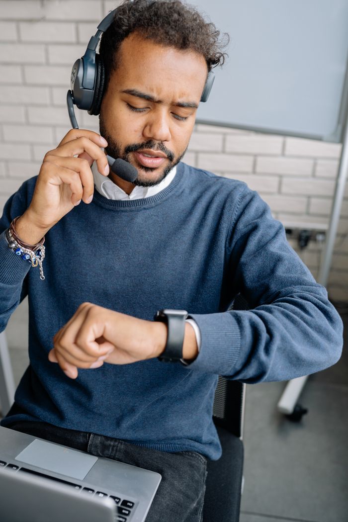 Professional call center employee speaking on headset while checking time indoors.